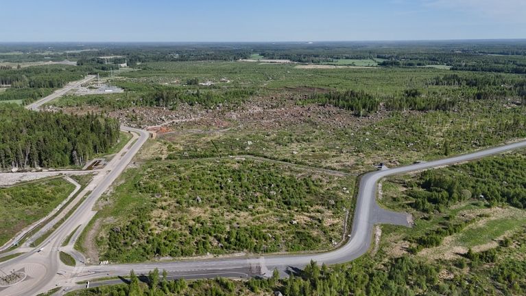 Aerial view of scrubby fields, a forest and a few roads.