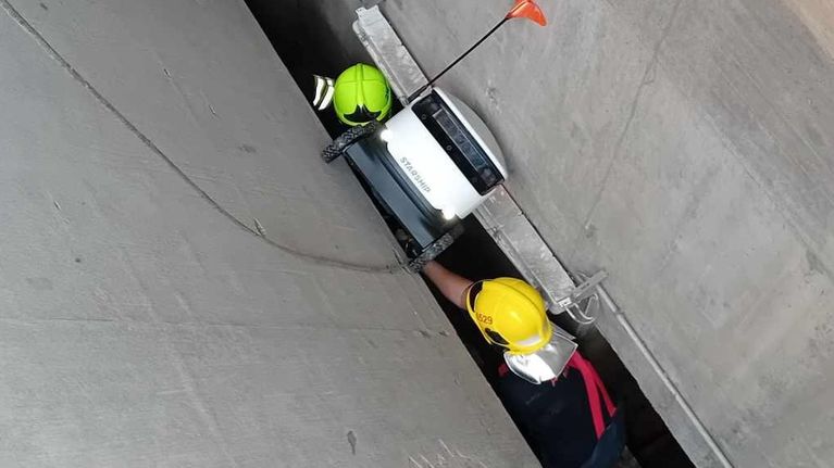 Kaksi kypäräpäistä henkilöä tarkastelee betonirakenteessa olevaa laitetta.