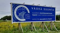 Sininen mainostaulu, joka kertoo missä Alajärven huutokaupattavat tontit ovat. Taulussa lukee "Väärä suunta"