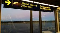 Tyhjä lentokenttä kiitoratoineen näkyy lentoaseman ikkunoista, kuvassa myös lähtevän liikenteen ja turvatarkastuksen kyltit.