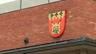 Punatiilinen seinä, johon on kiinnitetty ilvesaiheinen vaakuna.