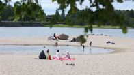 Personer njuter av en solig dag på stranden, där några leker vid vattenbrynet medan andra kopplar av på filtar på sanden.