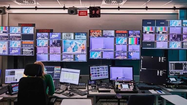 Nainen ohjaamossa edessään paljon näyttöjä, joissa tv-uutiset.