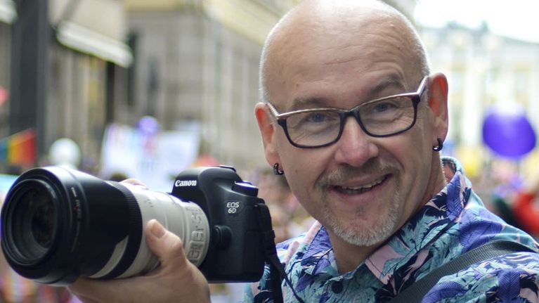 A man with glasses holding a camera. On top of the image the text "I have been able to use my skills often and in many ways, not only as a filmmaker and editor, but also as an interpreter and translator, as well as a player in radio and TV programmes." Berislav, cinematographer, video editor.