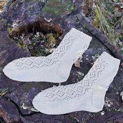 Handstickade strumpor med spetsmönster ligger ovanpå en gammal trädstubbe i naturen.