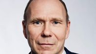 Keski-ikäinen mies tumma puku päällä ja kravatti kaulassa katsoo kameraan päin.