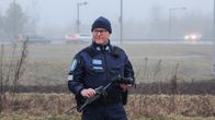 Poliisiasuinen miespoliisi seisoo autotien vieressä drooni kädessään.