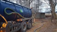 Sininen jätepuhdistamon säiliöauto ja syksyinen, puinen maasto takana.