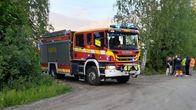En brandbil på en sandväg mellan två björjar i ett försommarlandskap. En bit därifrån står kanske ett tiotal människor  en klunga.