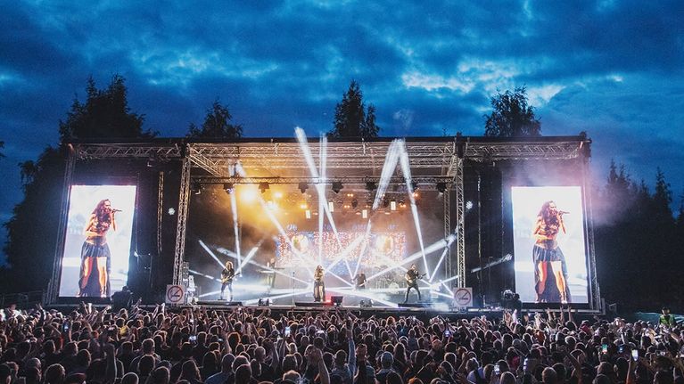 Yleisöä pakkautuneena lavan eteen ulkoilmakonsertissa illalla.