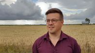 Silmälasipäinen mies seisomassa pellolla eteläpohjalaisen lakeuden keskellä, taustalla heinälato.