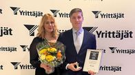 Nainen ja mies seisovat kukkakimpun ja palkinnon kanssa Yrittäjät-standin edessä.