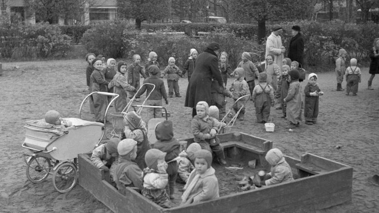 Vanha kuva, jossa paljon lapsia hiekkalaatikolla. 