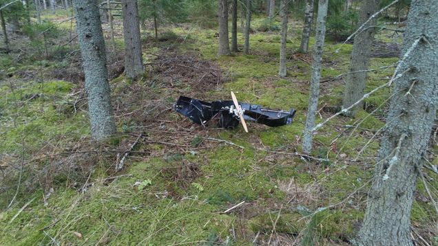 A pile of metal wreckage from a crashed drone lying on the ground in a forest.