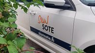 Oikealla valkoinen auto, jonka kyljessä lukee Siun sote. Vasemmalla pensas.
