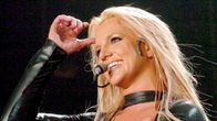 Britney Spears laulaa mustassa lateksipuvussa, ilme on iloinen.