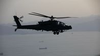 Amerikansk AH-64 Apache-attackhelikopter i luften, i bakgrunden syns skepp i Hormuzsundet.