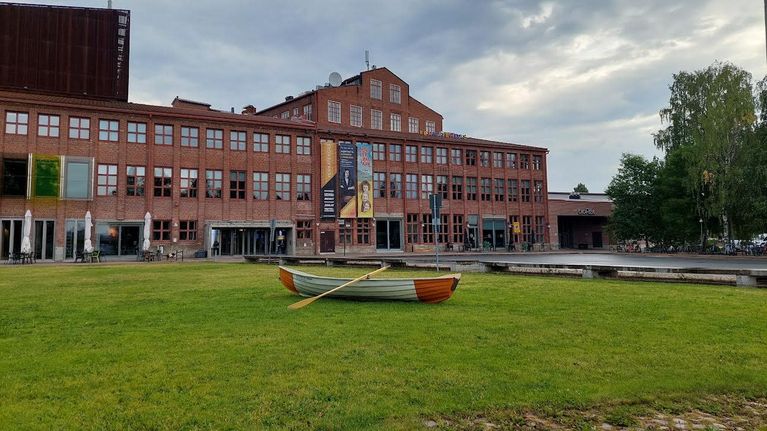 Soutuvene on keskellä nurmikkoa ison rakennuksen edessä.