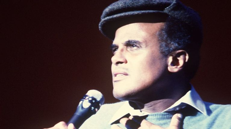 Harry Belafonte laulaa seisten, kohdevalo suunnattu laulajan kasvoille. Miehellä on lyhytlippainen hattu päässä.