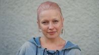 Kuvassa Christel Roosberg seisoo vaalean seinän edessä ja katsoo kameraan.