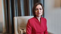Moldaviens president Maia Sandu i röd kavaj sitter i en ljus fåtölj i ett rum med grå gardiner.