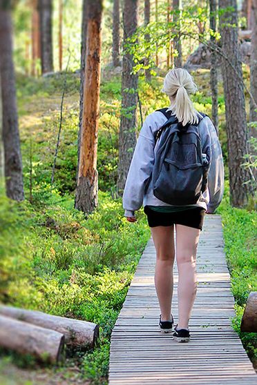 Nainen kävelee metsässä pitkospuilla, kuvan päällä on YKI-teksti.