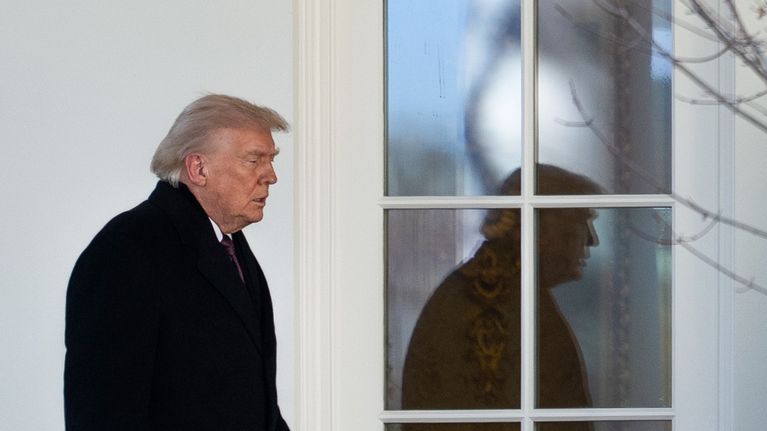 Donald J Trump menossa rakennukseen. Hänen kuvansa heihjastuu ikkunasta.