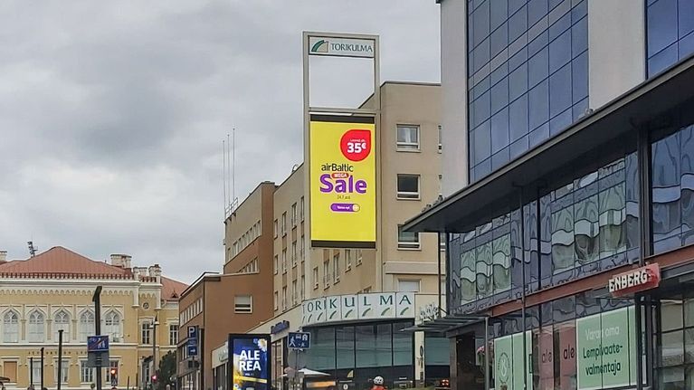 Jyväskylän Torikulman rakennuksen seinässä lukee Torikulma, ja siihen asennetussa valotaulussa mainostaa Air Baltic. Taustalla näkyy Jyväskylän vanha lyseo. Kävelykadulle on pysäköity polkupyöriä. 