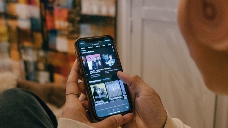 En flicka med hörlurar tittar på Yle Arenan i mobilen.