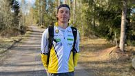 Ung man med en jacka fylld med reklam står på en skogsväg, han tittar in i kameran. 