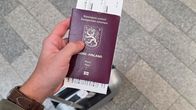 A hand holding a reddish-brown passport with an airline ticket inside it, seen from above.