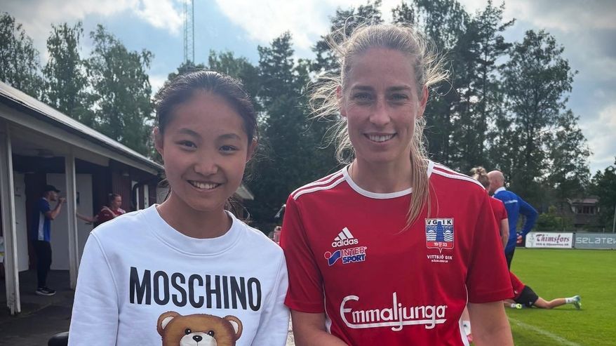 Fotbollsspelarna Queenie Xiang och Linda Sällström poserar för kameran vid en fotbollsplan.