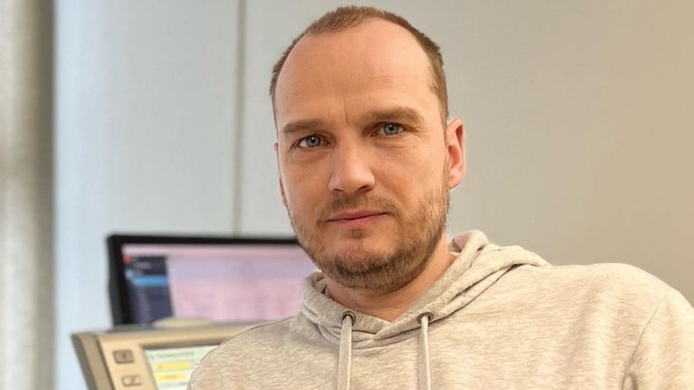Personporträtt på mansperson i kontorsmiljö. Mannen, klädd i ljusgrå huvtröja, tittar in i kameran.