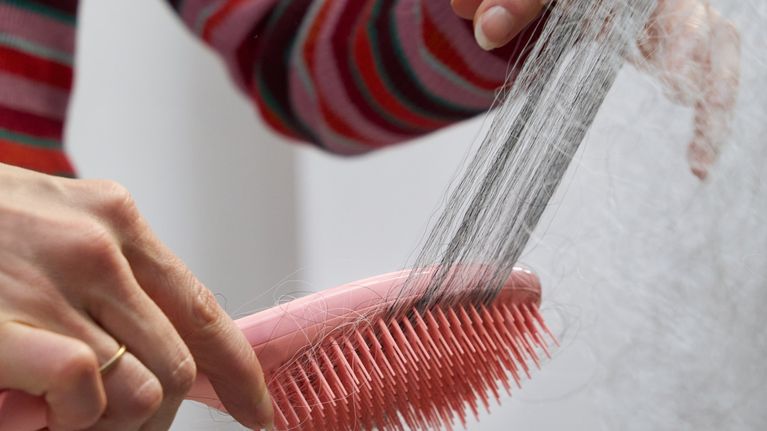 Närbild på person som håller i en rosa hårborste av plast som kammas igenom långt grått hår.