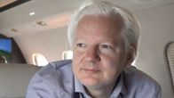 Julian Assange istuu lentokoneessa.