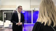 Silmälasipäinen ja siististi pukeutunut mies keskustelee naisen kanssa modernissa sisätilassa.