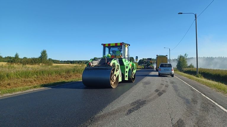 Päällystystyö, jyrä tasoittaa uutta asfalttia. Vieressä ohittavia autoja.