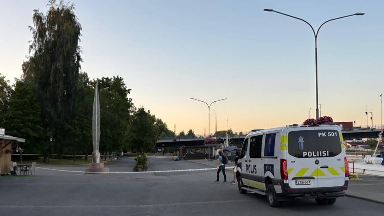 Poliisiauto ja poliisinauha sulkevat alueen sataman lähellä, taustalla näkyy puita ja veneitä. 