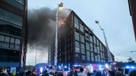 Kalasatamassa oleva kerrostalo tulessa. Ihmiset kadulla seuraavat sammutustöitä.