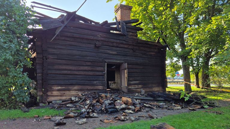 Timmerbyggnad som brunnit. Väggarna är svarta av branden och det ligger bråte framför huset. 