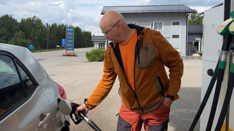 Jarmo Rasmus katsoo alaspäin, kun tankkaa autoon polttoainetta.