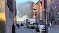 People standing in an urban street looking up at smoke pouring from a block of flats.