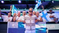En man står framför en grupp människor med finska flaggor.