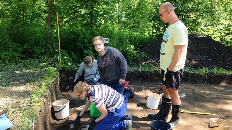 Vantaan Jokiniemen yleisökaivauksille osallistujat kaapivat maata, arkeologian opiskelija katselee