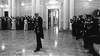 Tasavallan presidentin itsenäisyyspäivän vastaanotto Presidentinlinnassa 1975. Presidentti Urho Kekkonen seisoo yksin keskellä salia, taustalla vieraita ja valokuvaajia.