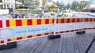 En avspärrning med informationsskyltar står uppställd på ett torg framför byggnader och bussar.