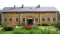 Vanha keltainen puutalo Suomessa kesäisen puutarhan ympäröimänä.