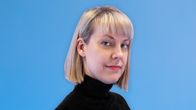 Vaaleahiuksinen polkkatukkainen nainen mustassa poolopaidassa katsoo suoraan kohti kameraa.