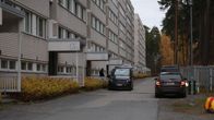 Ruumisauto ja poliisin siviiliauto kerrostalon edessä.