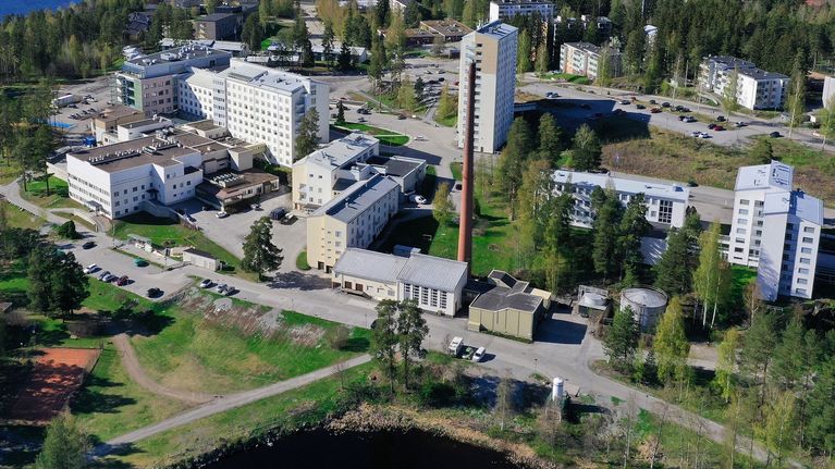 Kuvassa on kesällä ilmasta kuvattu Savonlinnan sairaala-alue, jonka keskellä näkyy korkea tiilipiippu.